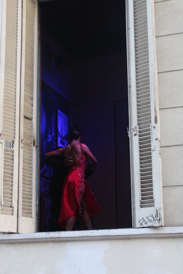 A dancer in a red dress performs tango inside a window in Buenos Aires, Argentina.