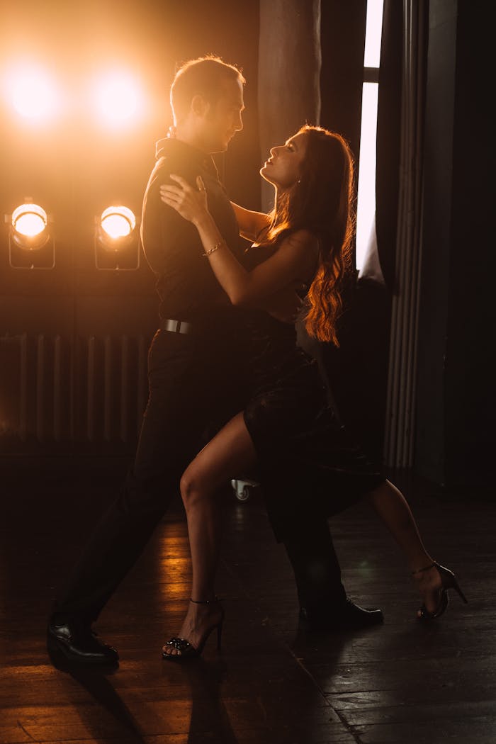 A couple gracefully dancing in a dimly lit ballroom, highlighted by dramatic lighting.